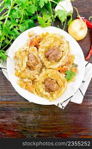 Twisted pasta with meatballs in the center with cream sauce, stewed tomatoes, bell peppers, onions and garlic in white plate on dark wooden board background from above