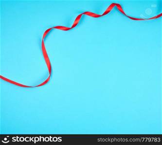 twisted red silk ribbon, blue background, top view, copy space