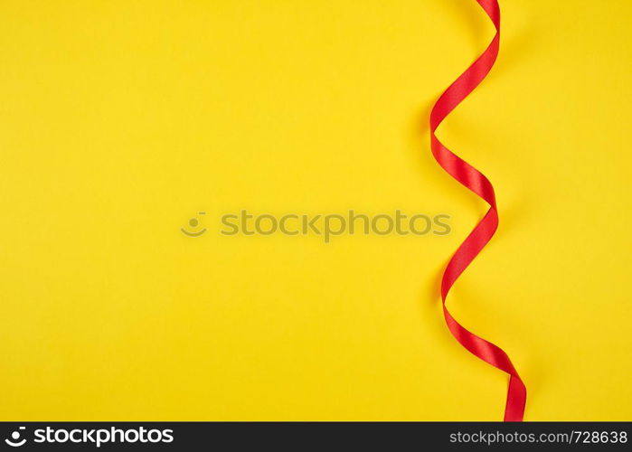 twisted red silk ribbon, yellow background, top view, copy space, holiday background