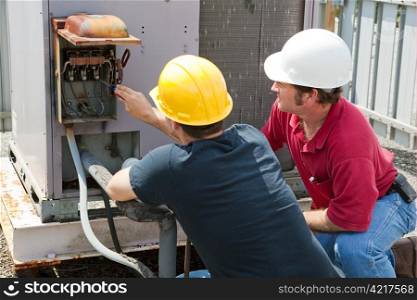 Two AC technicians repairing an industrial air conditioning compressor.