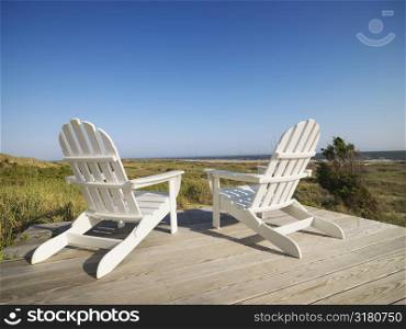 Two adirondack chairs on wooden deck overlooking beach at Bald Head Island, North Carolina.