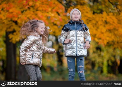 Two adorable little girls having fun in autumn forest outdoors. Little adorable girls at warm sunny autumn day outdoors