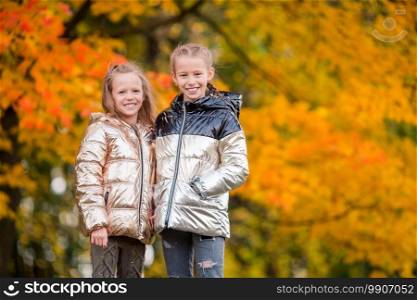 Two adorable little girls having fun in autumn forest outdoors. Little adorable girls at warm sunny autumn day outdoors