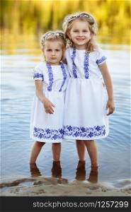 Two adorable little sisters laughing and hugging on warm and sunny summer day. two sisters in white dresses near the water. Two adorable little sisters laughing and hugging on warm and sunny summer day. two sisters in white dresses near the water.