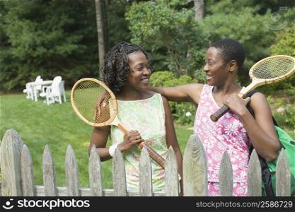 Two adult women holding tennis rackets and smiling in a lawn