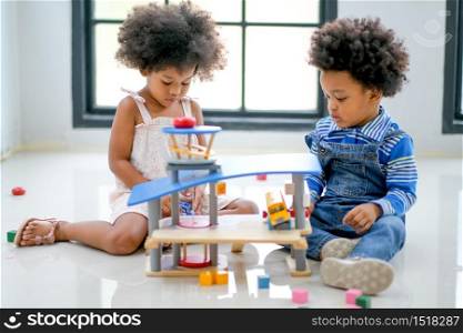 Two African brother and sister play some toys together in the room with day light with main focus on little girl.
