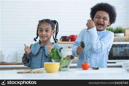 Two African cute sister and brother smiling, thumbs up cheering for eat fresh vegetables at home kitchen. Boy laughing and holding green salad vegetable in hand. Healthy food, good for kids