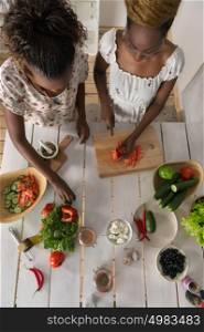 Two african women cooking in kitchen making healthy food salad with vegetables. Top view