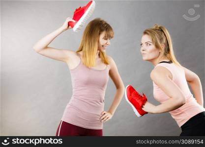 Two agressive women having argue fight using shoes being mad at each other. Female violance concept.. Two agressive women fighting using shoes
