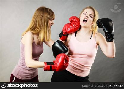 Two agressive women wearing boxing gloves having argue fight being mad at each other. Female violance concept.. Two agressive women having boxing fight