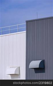 Two air ducts ventilation on grey and white corrugated metal factory buildings wall with blue sky in vertical frame