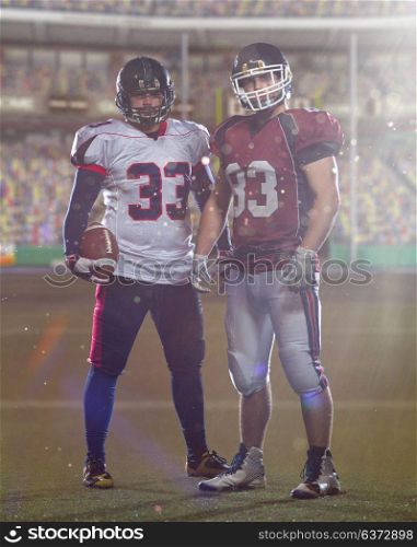 Two American football players standing on the field of big modern stadium with flares and lights