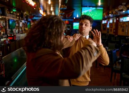 Two angry friends quarreling and fighting at sport bar. Furious soccer fans grimacing and pushing each other. Two angry friends quarreling with each other fighting at sport bar