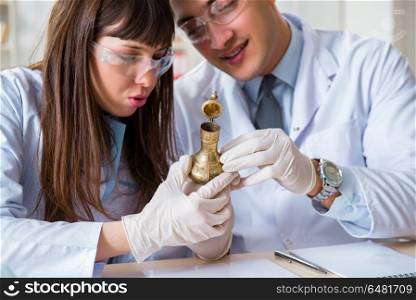 Two archeologists looking at ancient gold lamp