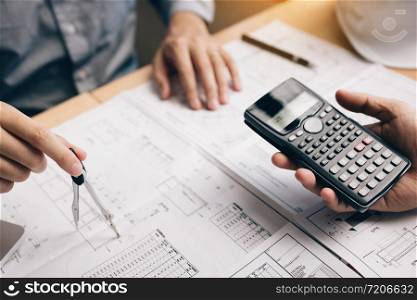 Two architect working at construction site and compass drawing pointing on blueprint with calculator calculate.