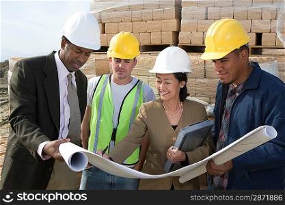 Two architects and two construction workers standing on construction site holding blueprints