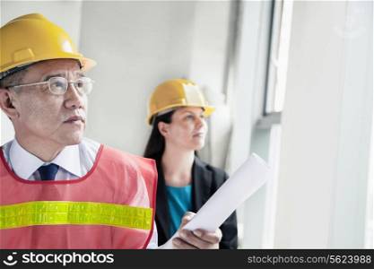Two architects in protective workwear and hardhats working in an office building
