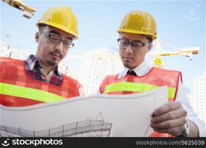 Two architects looking at a blueprint outdoors at a construction site