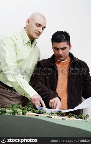 Two architects standing near a model and discussing a blueprint