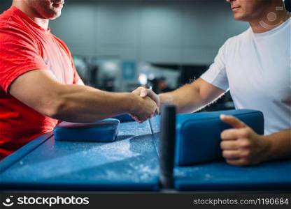 Two arm wrestlers shake hands after battle or wrestling competition, gym interior on background. Wrestle challenge, power sport