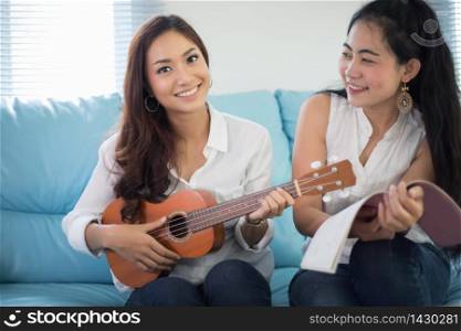 Two asia women are having fun playing ukulele and smiling at home for relax time
