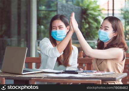 Two asian business woman wearing mask and being happy after getting success on their job