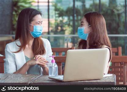 Two asian business women wearing mask and washing hands by gel before working. New Normal and Business Concept.