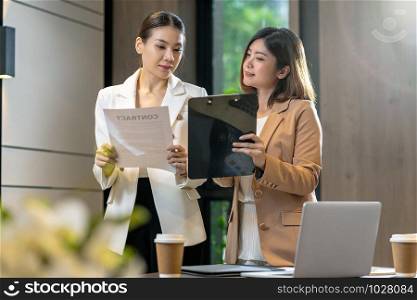 Two asian businesswomen discussing with the partner business about business contract by technology laptop in modern meeting room, office or working space, coffee break, partner and colleague concept