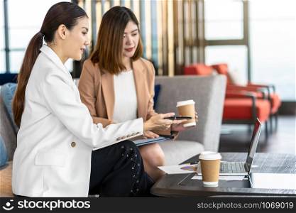 Two asian businesswomen discussing with the partner business with technology laptop during coffee break in modern office or coworking space, coffee break, relaxing and talking, partner and colleague