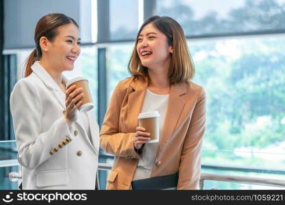 Two asian businesswomen talking during coffee break in modern office or coworking space, coffee break, relaxing and talking after working time, business and people partnership concept