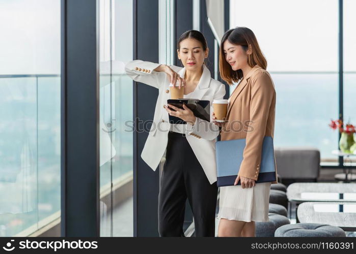 Two asian businesswomen talking during coffee break in modern office or coworking space, coffee break, relaxing and talking after working time, business and people partnership concept