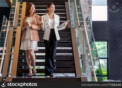 Two asian businesswomen walking and talking during coffee break in modern office or coworking space, coffee break, relaxing and talking after working time, business and people partnership concept