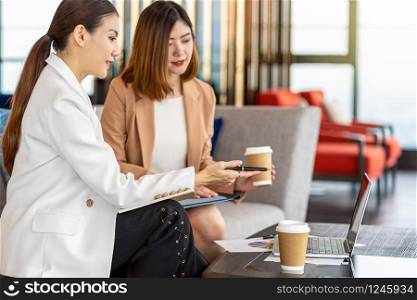 Two asian businesswomen working with the partner business by point pen to the technology laptop in modern office or coworking space,coffee break,partner and colleague,discussion and brainstorm concept