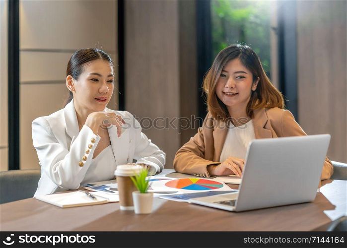 Two asian businesswomen working with the partner business via technology laptop in modern meeting room, office or working space, coffee break, partner and colleague concept