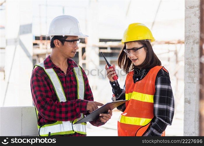 Two Asian engineer foreman architect worker man and woman talking at building construction site, engineering hold radio discussion operate project and control worker employee to building construction