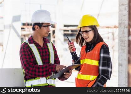 Two Asian engineer foreman architect worker man and woman talking at building construction site, engineering hold radio discussion operate project and control worker employee to building construction