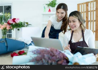 Two asian female florist working at flower shop with laptop.