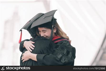 Two asian female students wearing uniform, cap and smiling, hug each other with happiness after graduation. Education Concept.