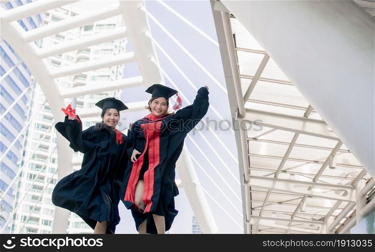 Two asian female students wearing uniform, cap, jumping and smiling with happiness after graduation. Education Concept.