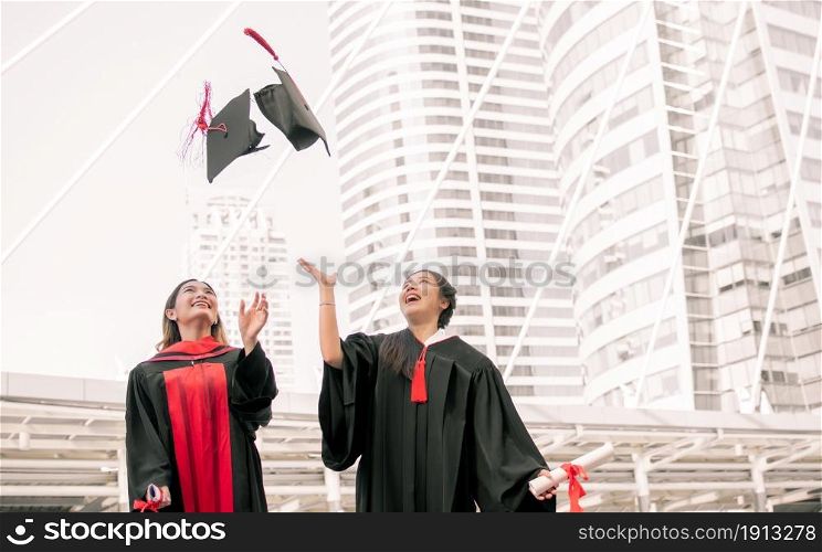 Two asian female students wearing uniform, smiling with happiness and throwing caps after graduation. Education Concept.
