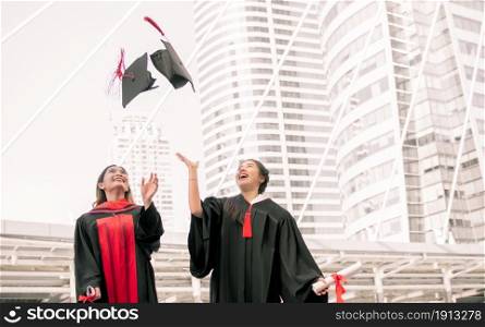 Two asian female students wearing uniform, smiling with happiness and throwing caps after graduation. Education Concept.
