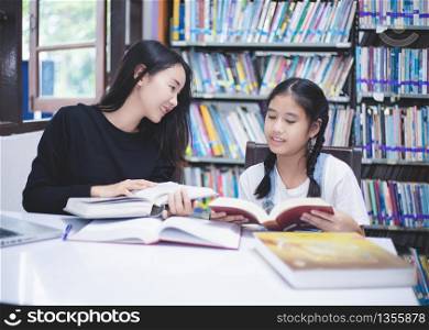 Two Asian girl students reading books and using notebook in the library.