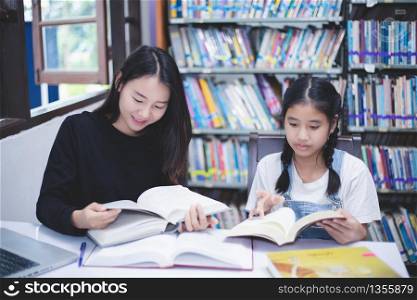 Two Asian girl students reading books and using notebook in the library.