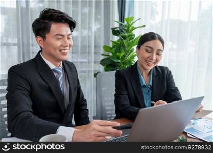 Two Asian office workers discussing and working together in corporate office workplace. Coworkers smiling and planning business work in friendly working environment in corporate workspace. Jubilant. Two Asian office workers working together in workplace. Jubilant