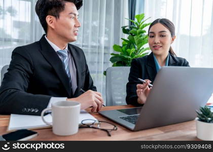 Two Asian office workers discussing and working together in corporate office workplace. Coworkers smiling and planning business work in friendly working environment in corporate workspace. Jubilant. Two Asian office workers working together in workplace. Jubilant