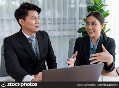 Two Asian office workers discussing and working together in corporate office workplace. Coworkers smiling and planning business work in friendly working environment in corporate workspace. Jubilant. Two Asian office workers working together in workplace. Jubilant