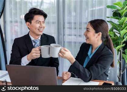 Two Asian office workers taking coffee break together in workplace. Coworkers smiling and socializing while holding cup of coffee adding friendly working environment in corporate workspace. Jubilant. Two Asian office workers taking coffee break together in workplace. Jubilant