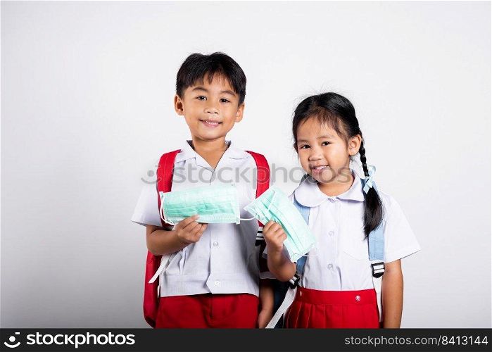 Two Asian student kid girl boy brother sister wearing student thai uniform holding protect mask ready to go to school in studio shot isolated on white background, new normal back to school