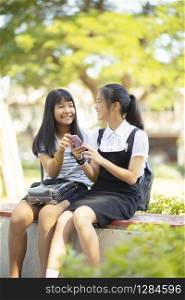 two asian teenager happiness face holding smartphone in hand talking wiht relaxing emotion