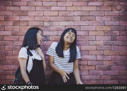two asian teenager laughing with happiness emotion standing against red brick wall